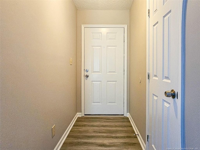 doorway with a textured ceiling, baseboards, and dark wood finished floors