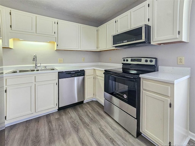 kitchen with a sink, light countertops, appliances with stainless steel finishes, a textured ceiling, and light wood-style flooring