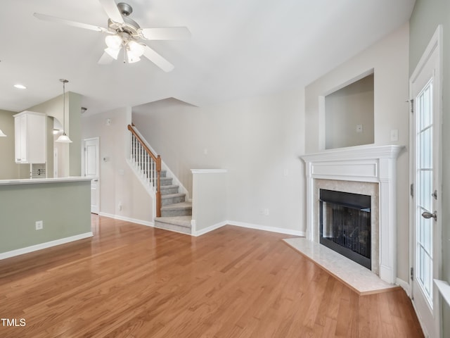 unfurnished living room with a ceiling fan, a high end fireplace, baseboards, light wood-style floors, and stairs