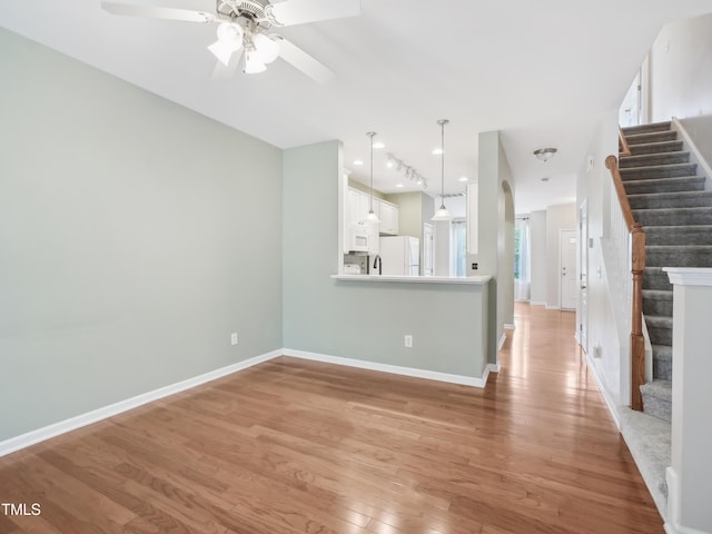 unfurnished living room featuring stairs, a ceiling fan, baseboards, and light wood-type flooring