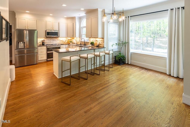 kitchen with a sink, a peninsula, appliances with stainless steel finishes, backsplash, and light wood-style floors