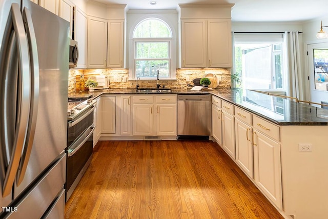 kitchen with a peninsula, appliances with stainless steel finishes, ornamental molding, and dark wood-style floors