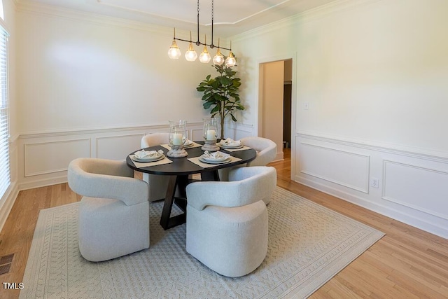 dining room with wood finished floors, a decorative wall, wainscoting, and ornamental molding