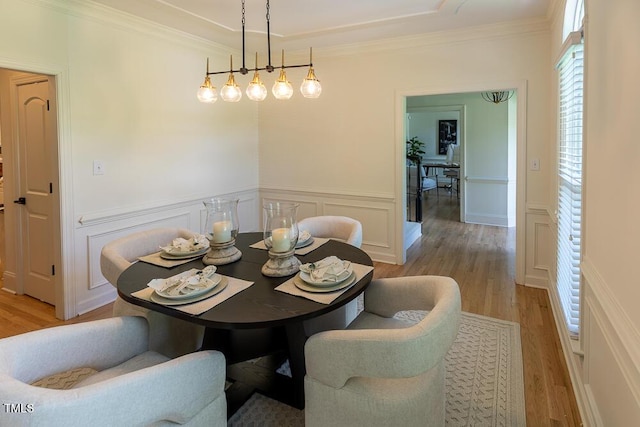 dining space featuring light wood-type flooring, a decorative wall, wainscoting, and ornamental molding