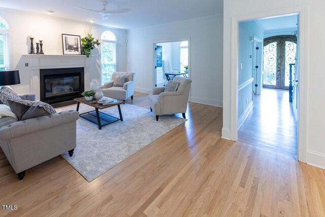living room with crown molding, a glass covered fireplace, french doors, a ceiling fan, and light wood-type flooring