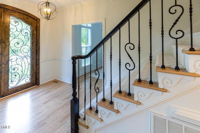 entrance foyer with wood finished floors, stairway, a chandelier, ornamental molding, and baseboards