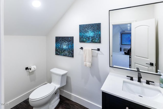 bathroom with lofted ceiling, baseboards, wood finished floors, toilet, and vanity