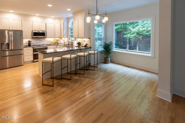 kitchen featuring appliances with stainless steel finishes, dark countertops, backsplash, a peninsula, and light wood finished floors