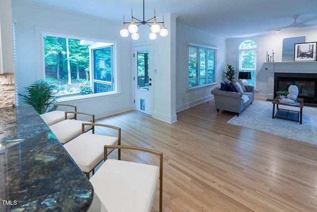 living room featuring light wood finished floors, ornamental molding, a glass covered fireplace, and baseboards