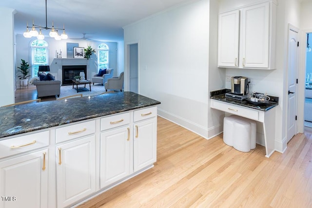 kitchen with light wood-type flooring, white cabinetry, dark stone countertops, and baseboards