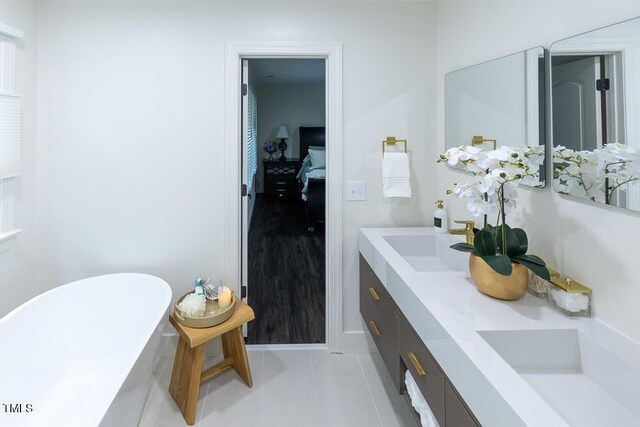 ensuite bathroom featuring a freestanding bath, tile patterned floors, double vanity, and baseboards