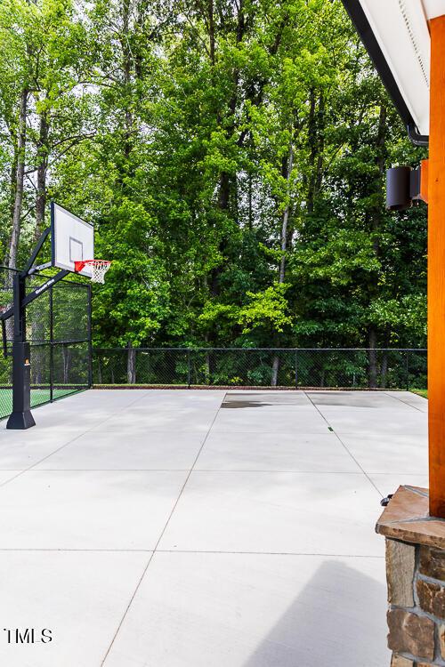 view of patio / terrace featuring community basketball court, fence, and view of wooded area