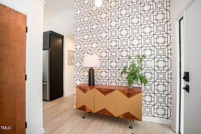 hallway featuring baseboards, light wood finished floors, and lofted ceiling
