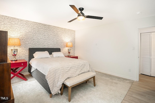 bedroom with ceiling fan, baseboards, an accent wall, and wood finished floors