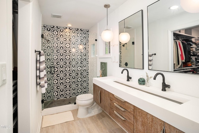 full bathroom with double vanity, toilet, a shower stall, visible vents, and wood finished floors