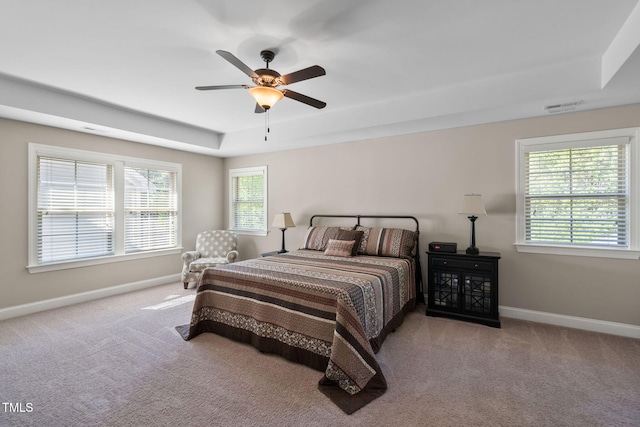carpeted bedroom featuring visible vents, ceiling fan, a tray ceiling, and baseboards