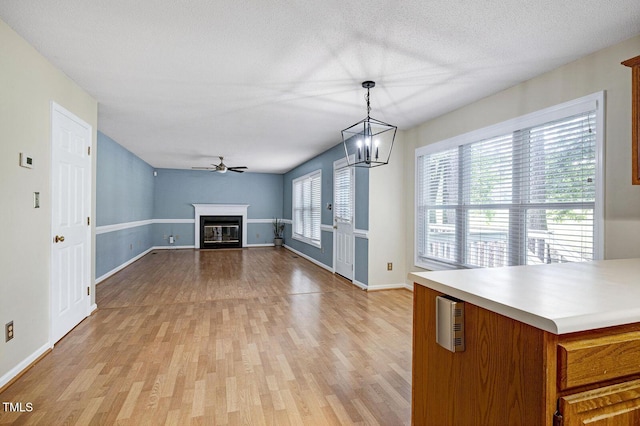 3900 Inkberry Ct, Apex, NC 27539 - unfurnished living room featuring light wood finished floors, a ceiling fan, a glass covered fireplace, a chandelier, and a textured ceiling