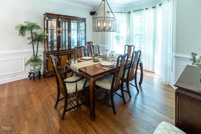 dining room with dark wood-style flooring, a wainscoted wall, an inviting chandelier, ornamental molding, and a decorative wall