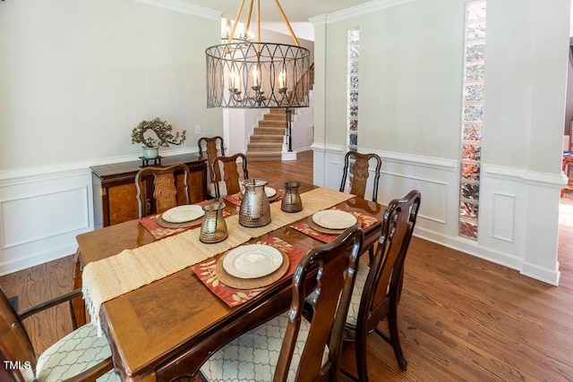 dining area featuring crown molding, a decorative wall, a chandelier, stairs, and wood finished floors