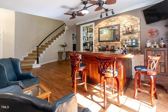bar featuring a bar, a ceiling fan, stairs, and wood finished floors