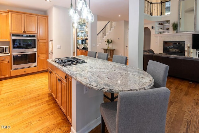 kitchen featuring a kitchen bar, appliances with stainless steel finishes, a center island, light stone counters, and light wood-style floors