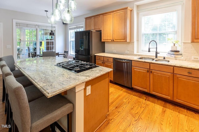 kitchen featuring light stone counters, a sink, light wood-style floors, a breakfast bar area, and stainless steel appliances