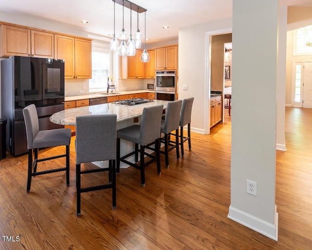 kitchen with a kitchen island, a breakfast bar, baseboards, light wood finished floors, and stainless steel appliances