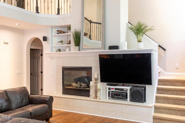 living area featuring a tiled fireplace, arched walkways, stairs, and wood finished floors