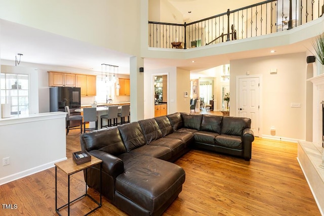 living room with a towering ceiling, a fireplace with raised hearth, baseboards, and light wood-type flooring