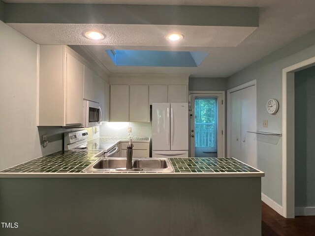 106 Orchard Rd, Henderson, NC 27536 - kitchen with white appliances, a peninsula, a skylight, a sink, and white cabinets