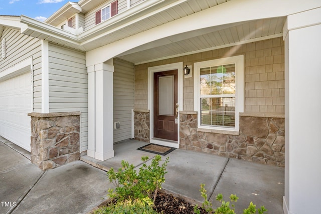 doorway to property featuring a porch, stone siding, and a garage
