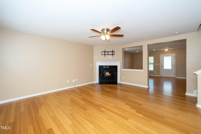 unfurnished living room with light wood-style flooring, a high end fireplace, a ceiling fan, and baseboards