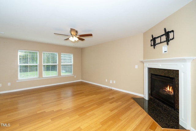 unfurnished living room with a high end fireplace, light wood finished floors, baseboards, and a ceiling fan