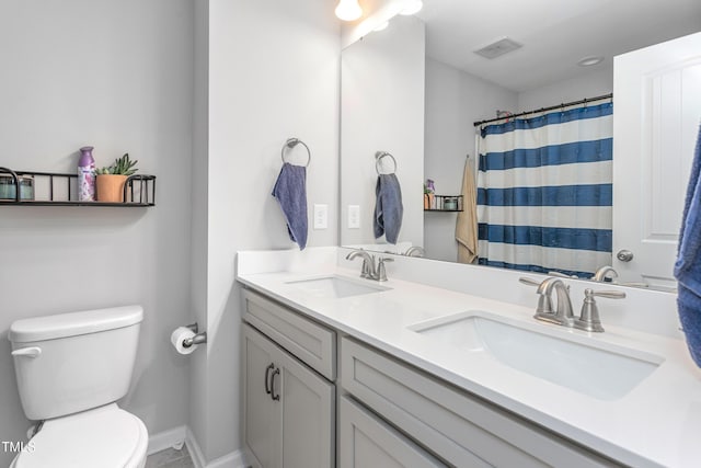 full bath featuring toilet, double vanity, a sink, and baseboards