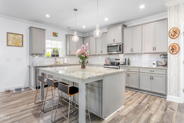 kitchen with crown molding, a kitchen breakfast bar, a kitchen island, gray cabinets, and appliances with stainless steel finishes