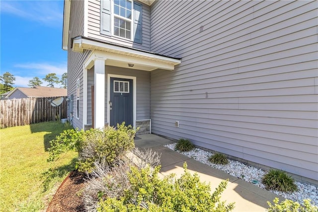 doorway to property featuring fence and a lawn