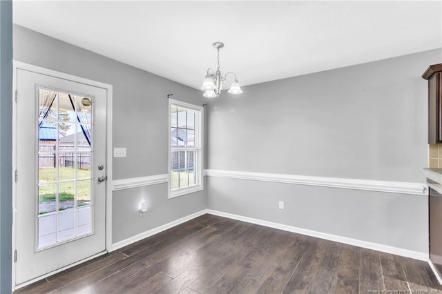 unfurnished dining area featuring a chandelier, a healthy amount of sunlight, baseboards, and dark wood finished floors