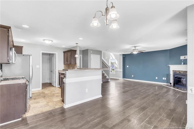 kitchen with ceiling fan with notable chandelier, a peninsula, wood finished floors, light countertops, and stainless steel appliances