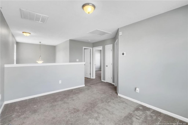 carpeted empty room featuring visible vents, baseboards, and attic access