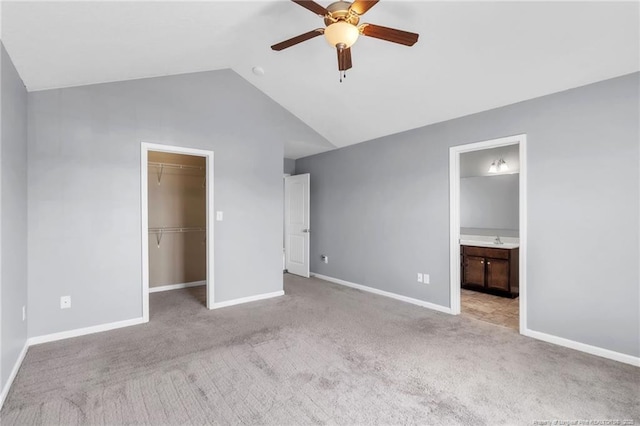 unfurnished bedroom featuring a walk in closet, light colored carpet, baseboards, and vaulted ceiling