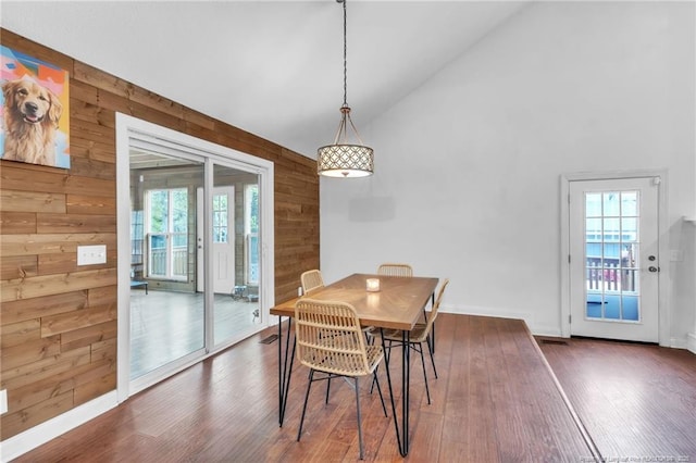 dining area featuring wood walls, dark wood finished floors, high vaulted ceiling, and a healthy amount of sunlight