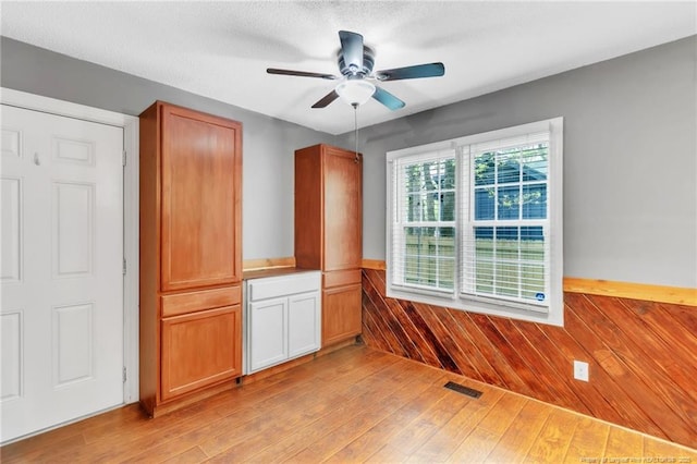 unfurnished room featuring wooden walls, a ceiling fan, visible vents, a wainscoted wall, and light wood finished floors