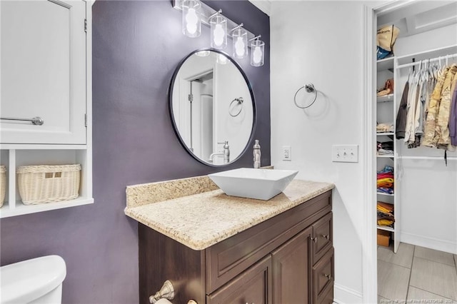 bathroom featuring toilet, vanity, baseboards, and a spacious closet