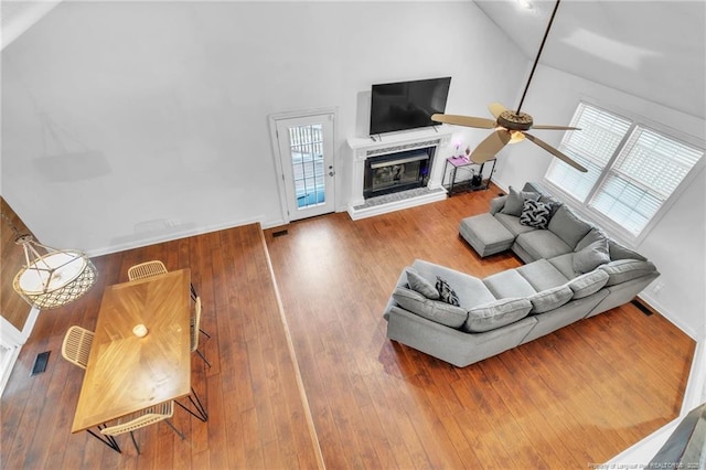 living room with high vaulted ceiling, a ceiling fan, visible vents, a glass covered fireplace, and hardwood / wood-style floors