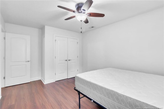 bedroom with a closet, a ceiling fan, visible vents, wood finished floors, and baseboards