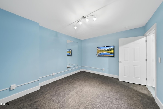 empty room featuring track lighting, dark colored carpet, and baseboards