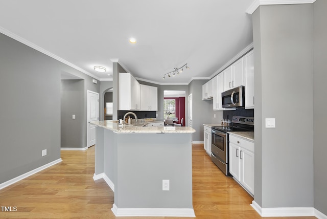 kitchen with light wood-style flooring, backsplash, white cabinets, appliances with stainless steel finishes, and arched walkways