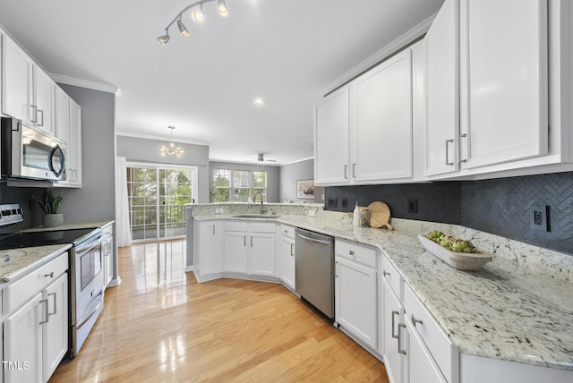 kitchen featuring ornamental molding, a peninsula, white cabinets, appliances with stainless steel finishes, and a sink