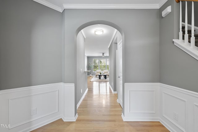 hallway featuring ornamental molding, light wood-style flooring, arched walkways, and a wainscoted wall
