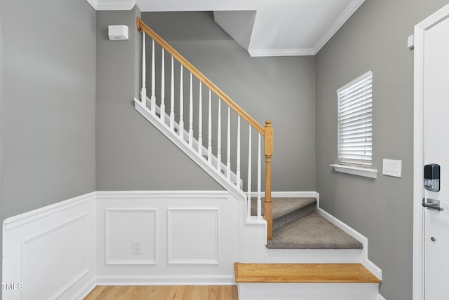 stairway featuring a decorative wall, wainscoting, crown molding, and wood finished floors